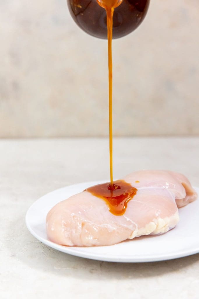 chicken breast on a white plate teriyaki sauce being poured on chicken