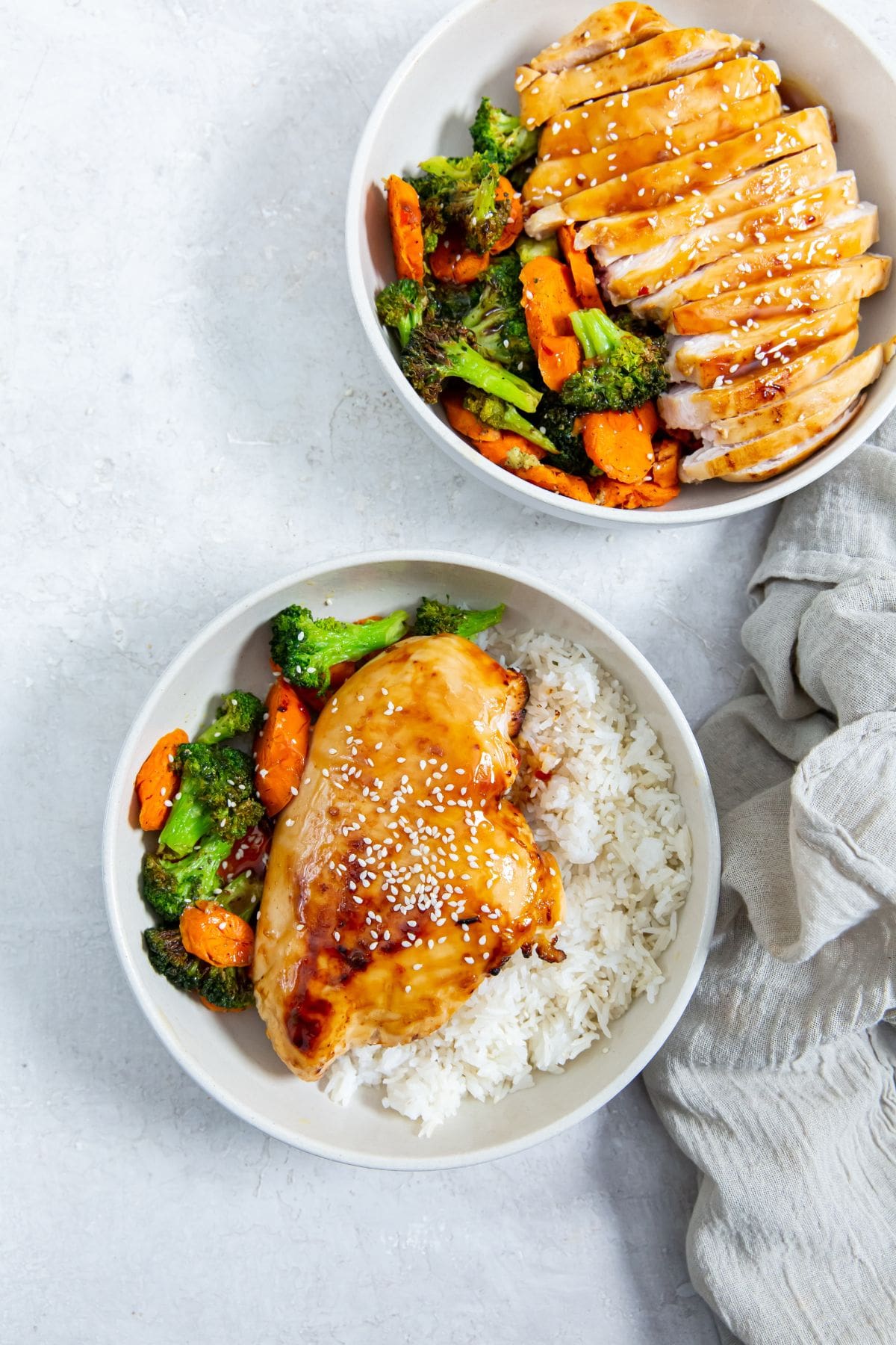 white bowls with chicken. veggies, and rice gray towel next to it