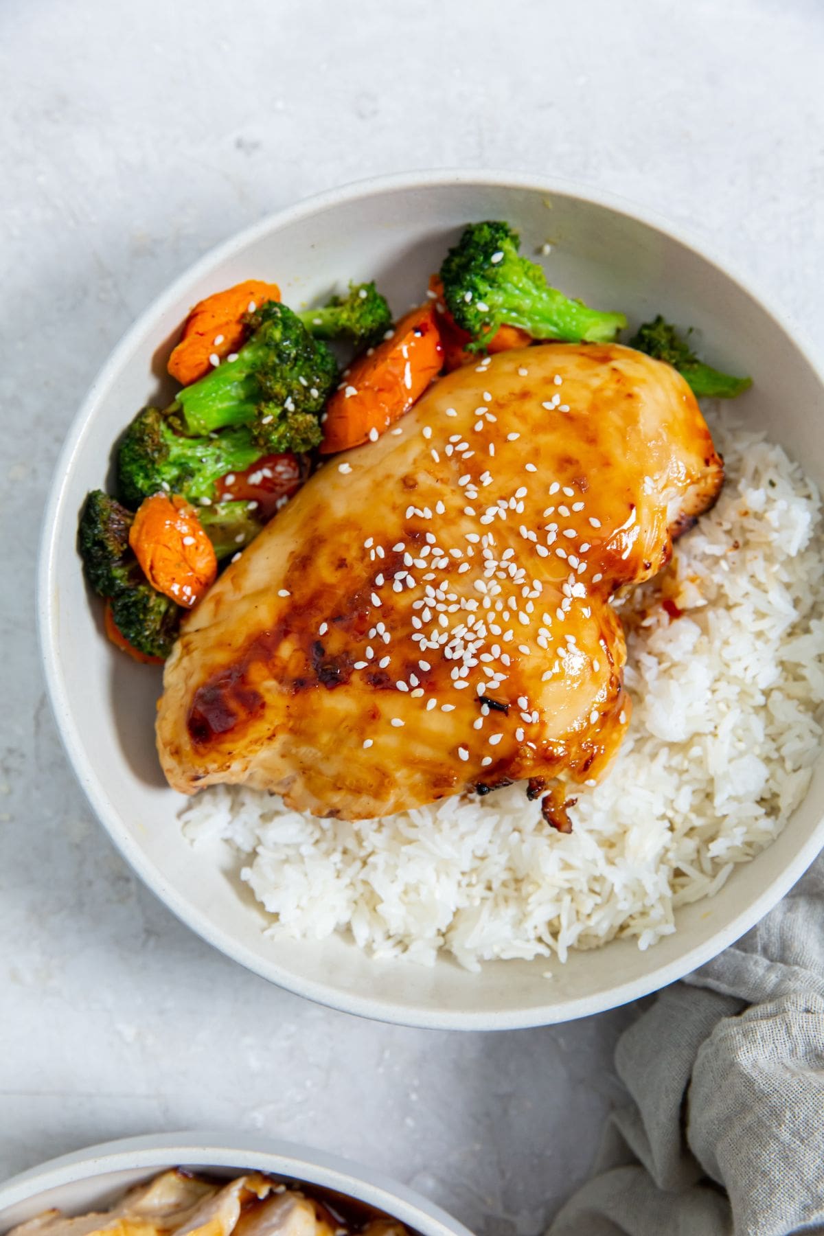 white bowl with chicken veggies and rice inside. gray towel next to it