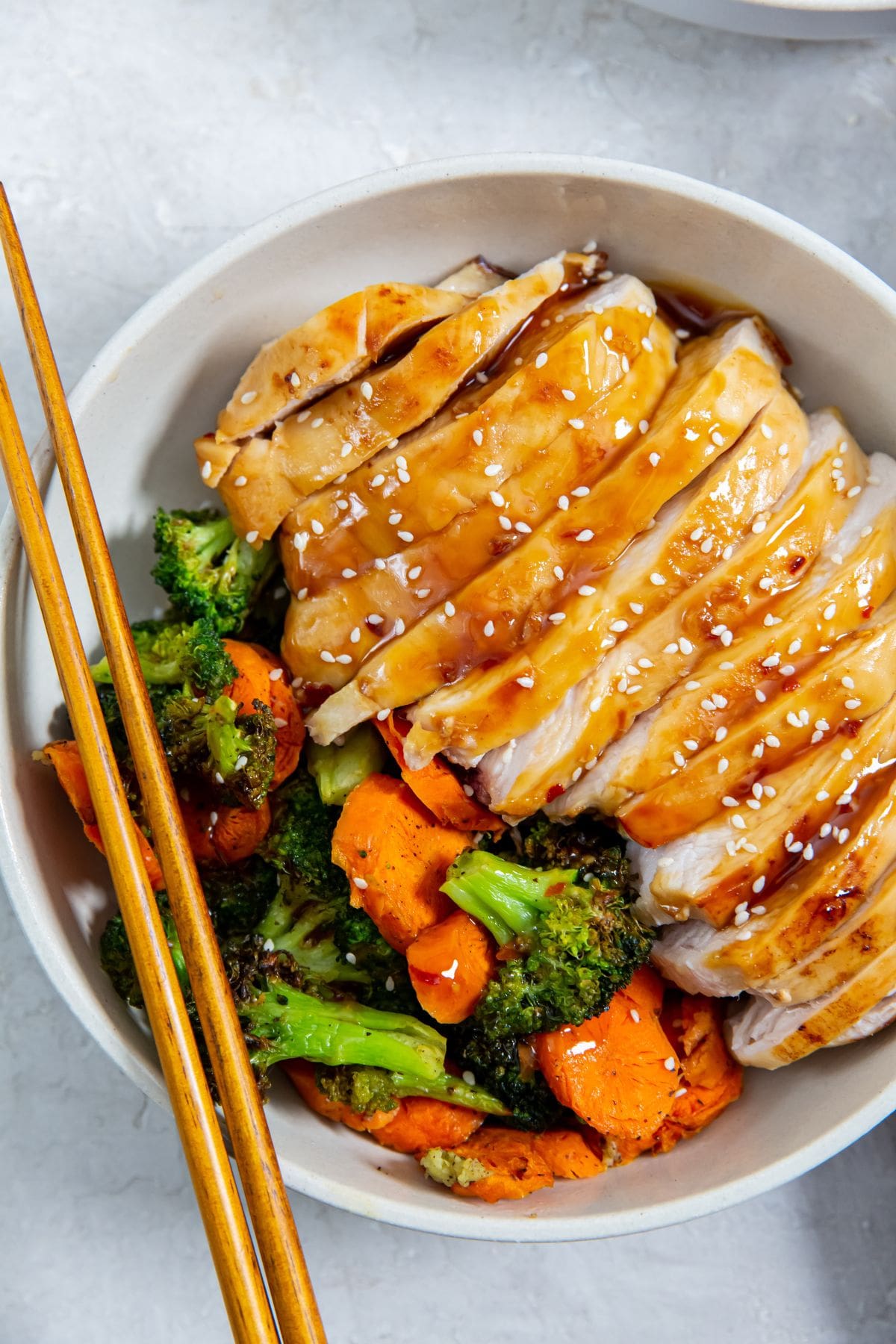 white bowl with chicken veggies and rice inside. gray towel next to it. Chopsticks on bowl