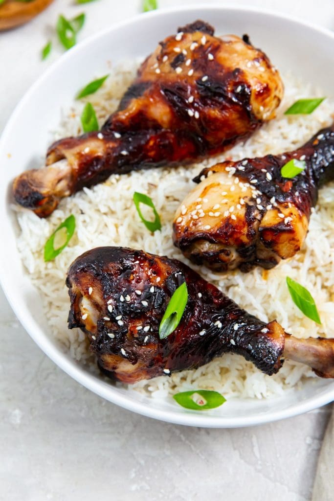 white bowl with rice and chicken legs inside. green onions in the back. Green towel next to bowl.