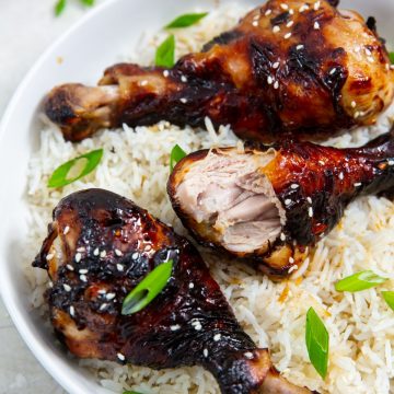 white bowl with rice and chicken legs inside. green onions in the back. Green towel next to bowl.