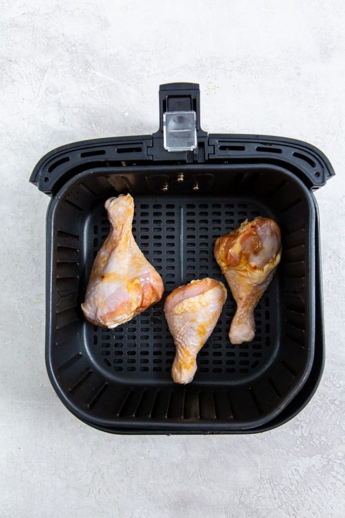 black air fryer basket with raw chicken legs inside