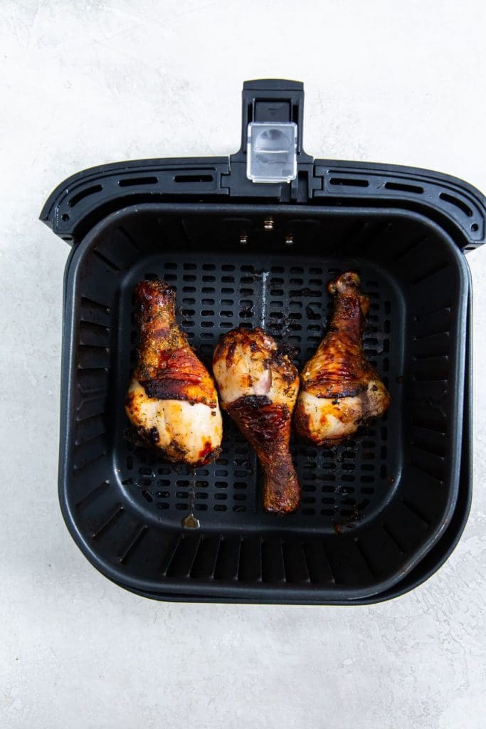 black air fryer basket with cooked chicken legs inside