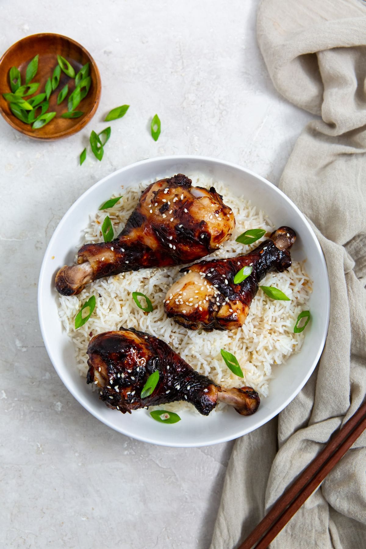 white bowl with rice and chicken legs inside. green onions in the back. Green towel next to the bowl. chopsticks on top of the towel.