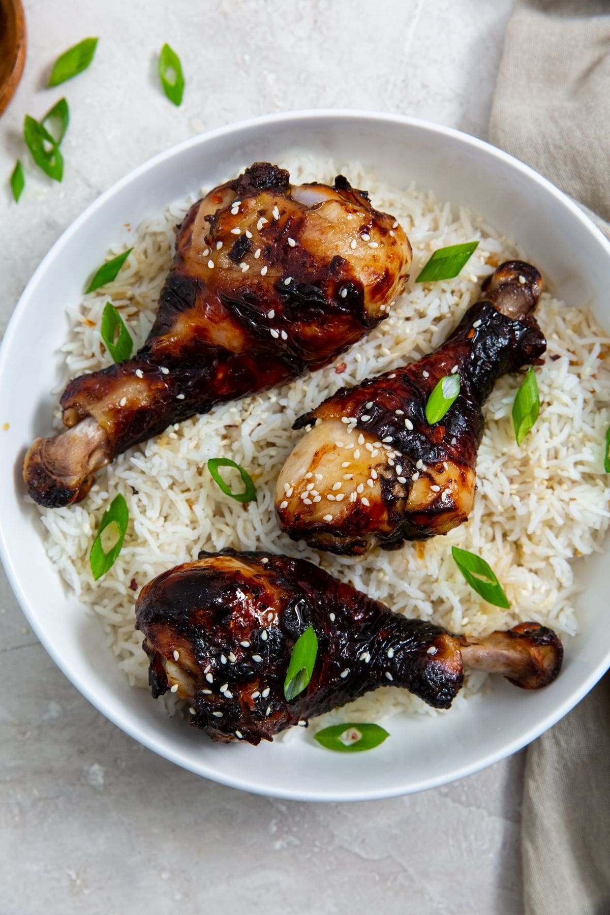 white bowl with rice and chicken legs inside. green onions in the back. Green towel next to bowl.