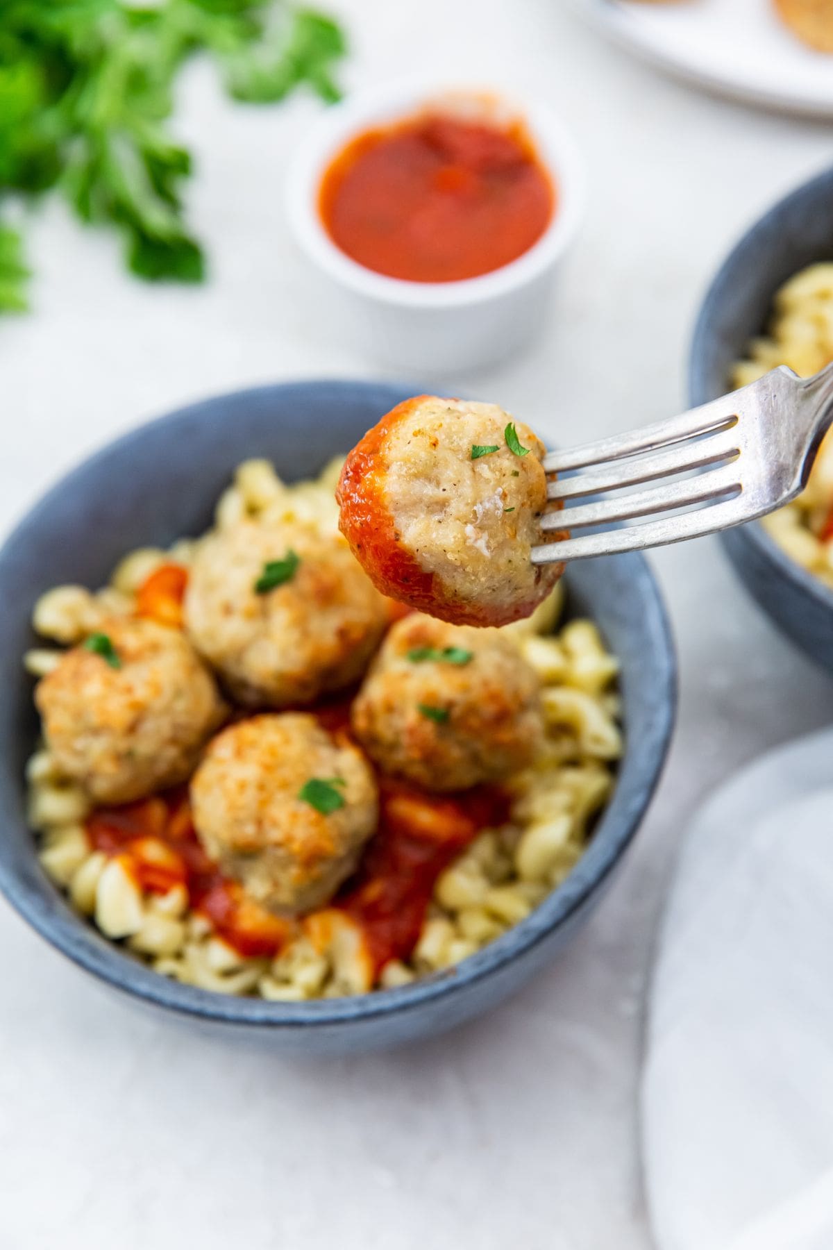 blue bowls with pasta and meatballs on top. sauce inn the back fork holding one meatball