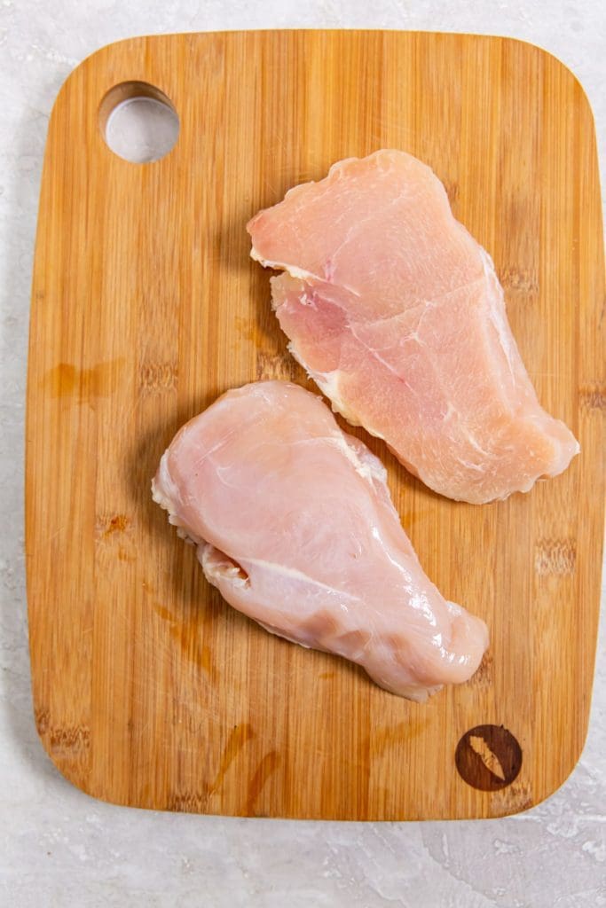 brown cutting board with chicken breast cut in half