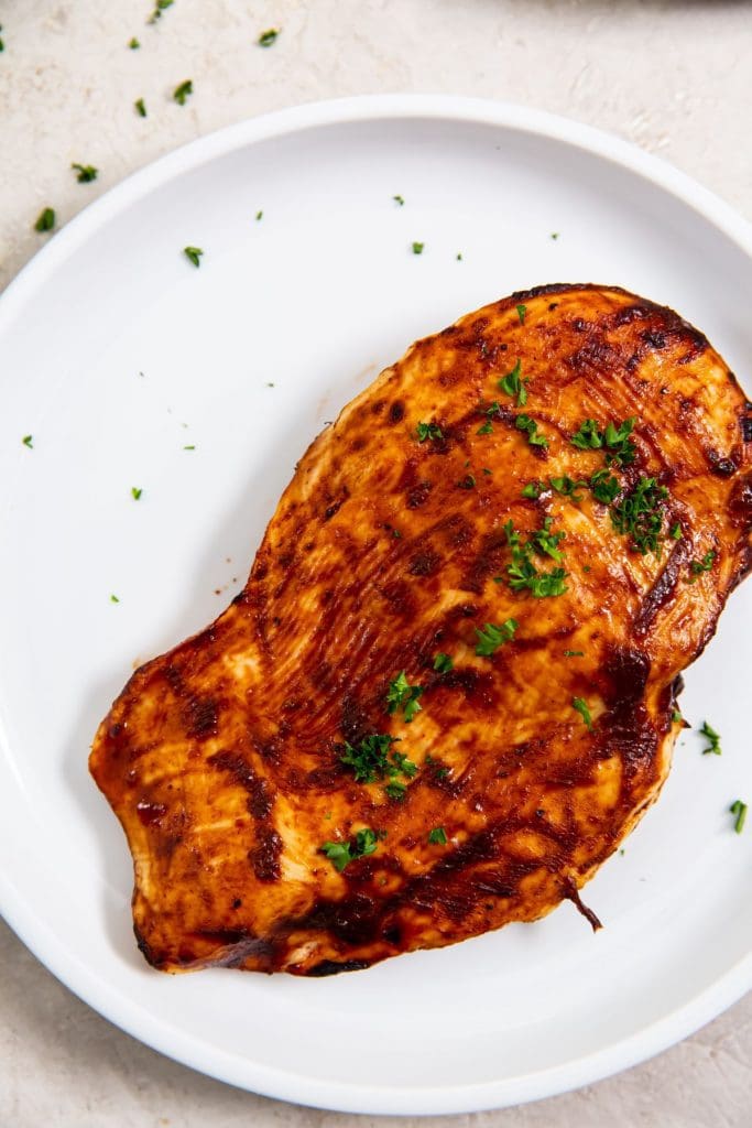 white plate with bbq chicken on it parsley on top