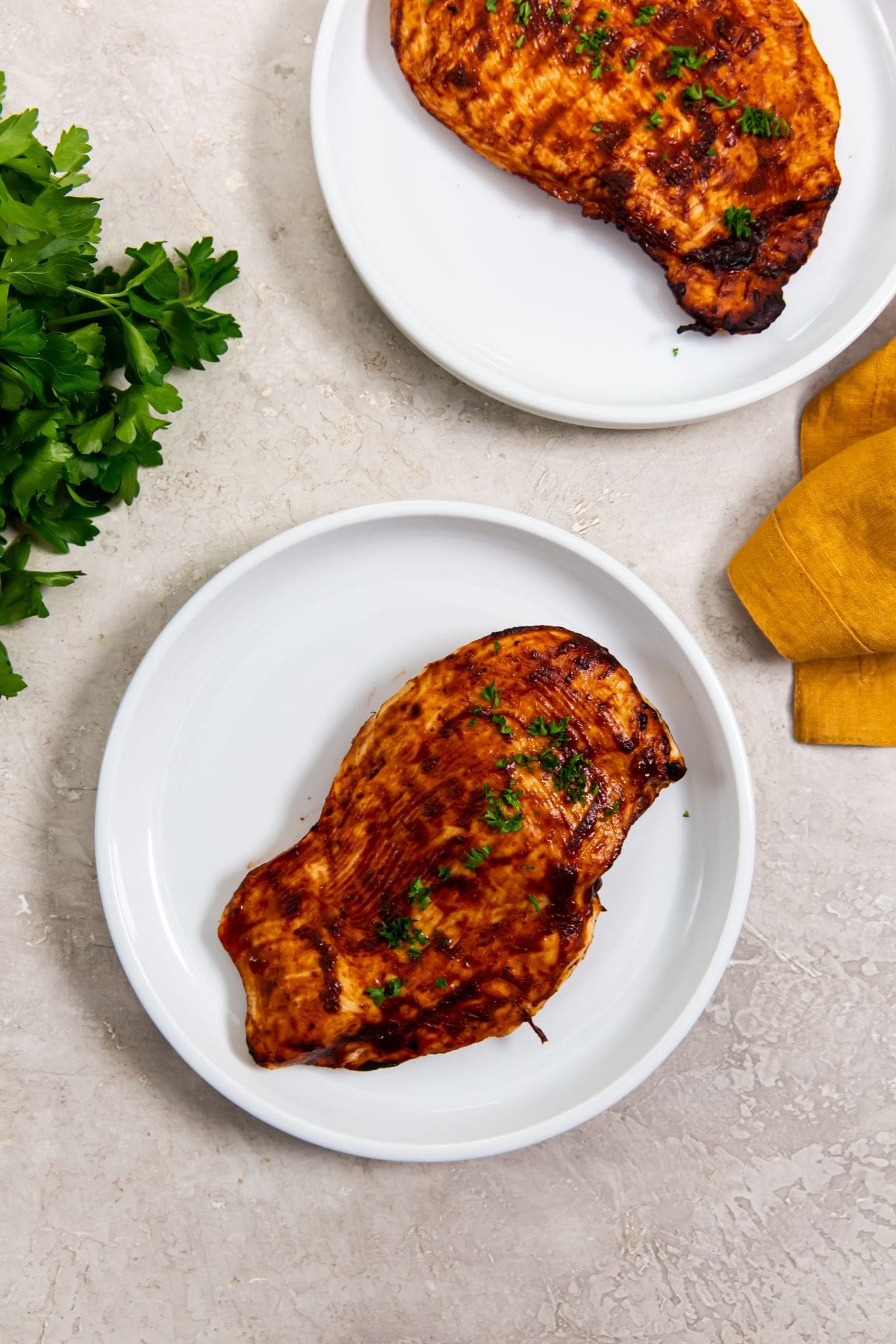 white plate with bbq chicken on it parsley on top parsley and yellow towel in the back