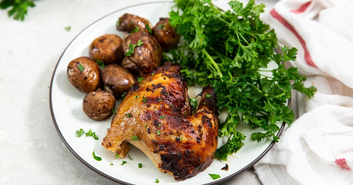 chicken cut with parsley and mushrooms on a white plate. white and pink towel next to it