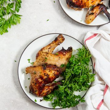 chicken cut with parsley on a white plate. white and pink towel next to it