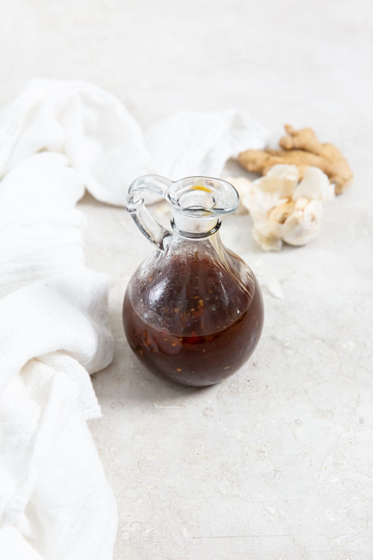 glass dressing bottle with teriyaki sauce inside white napkin in the back along with fresh garlic and ginger