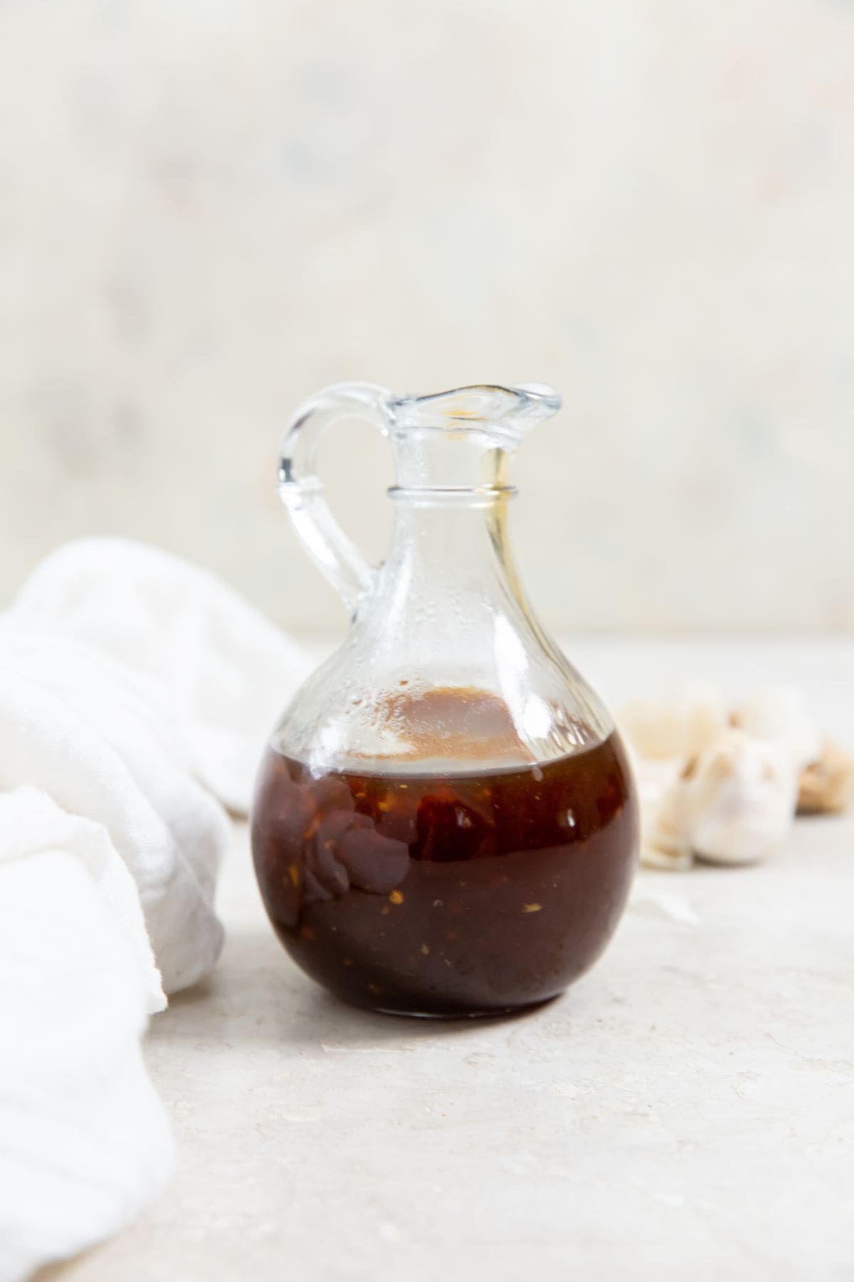 glass dressing bottle with teriyaki sauce inside white napkin in the back along with fresh garlic and ginger