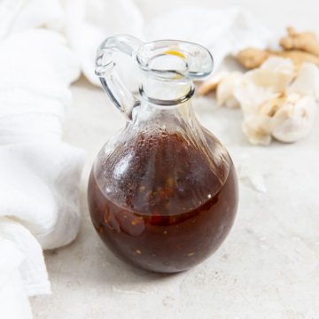 glass dressing bottle with teriyaki sauce inside white napkin in the back along with fresh garlic and ginger