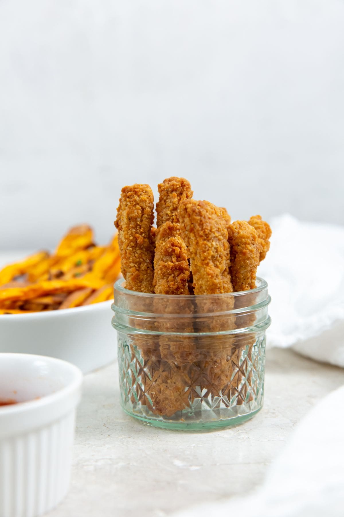 chicken fries inside a mason jar ketchup up front and sweet potatoes in the back. white towel next to it