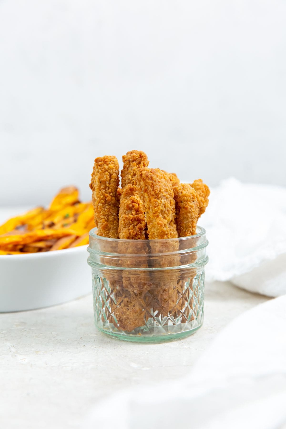 chicken fries inside a mason jar ketchup up front and sweet potatoes in the back. white towel next to it