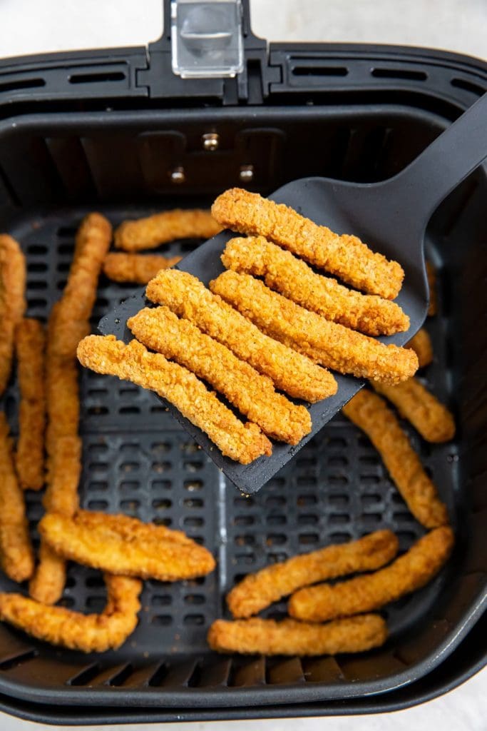 chicken fries inside black air fryer spatula holding some up