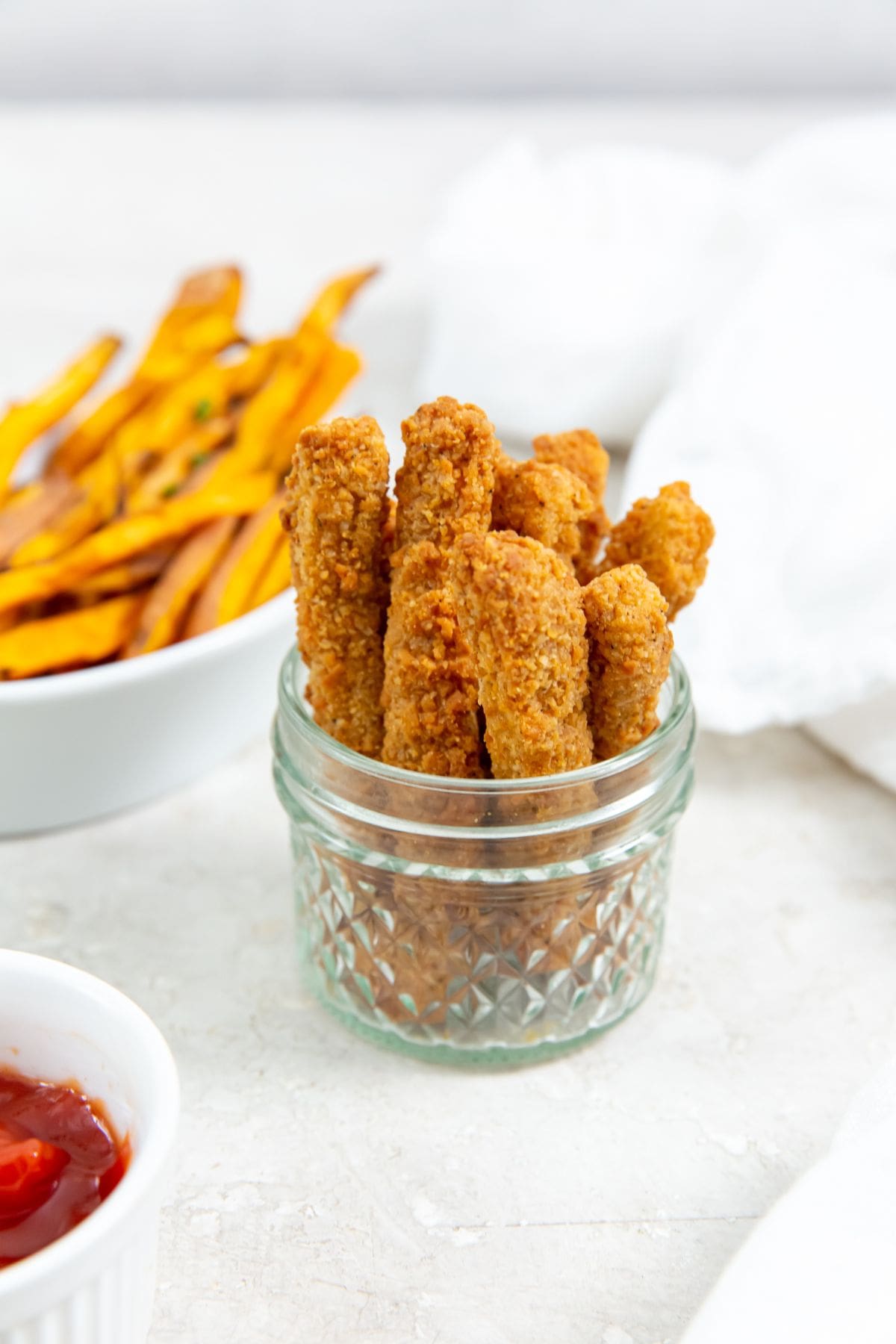 chicken fries inside a mason jar ketchup up front and sweet potatoes in the back. white towel next to it