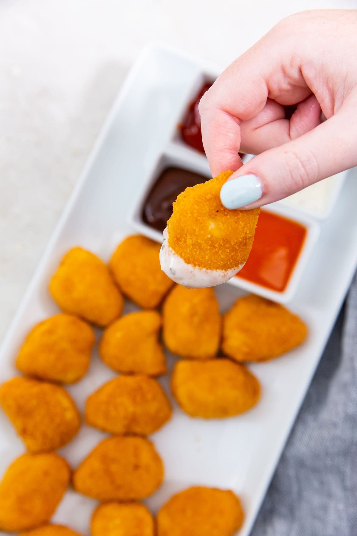 white plate with chicken nuggets dipping sauce in the back(buffalo, ranch, ketchup, and bbq) one nugget has ranch on it