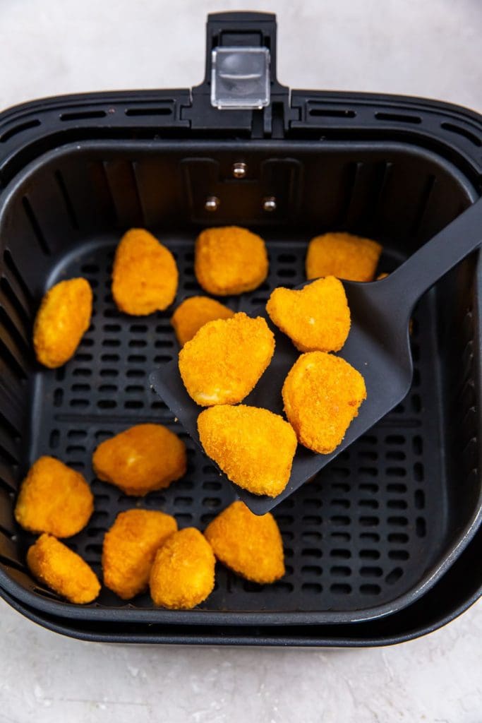 black air fryer with cooked nuggets inside. spatula holding nuggets