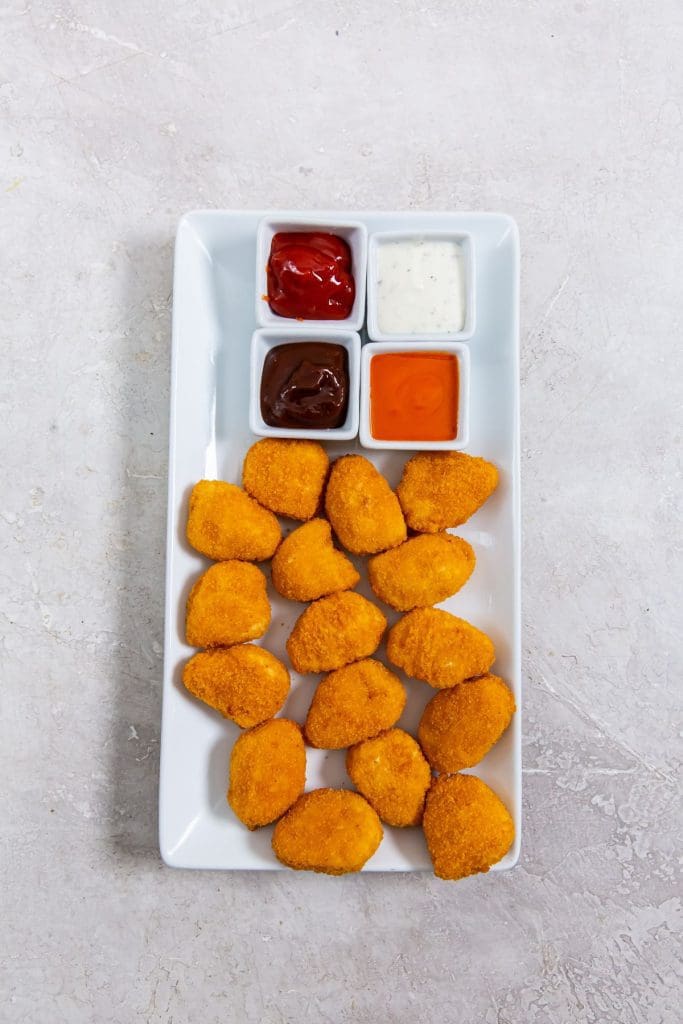 white plate with chicken nuggets dipping sauce in the back(buffalo, ranch, ketchup, and bbq)