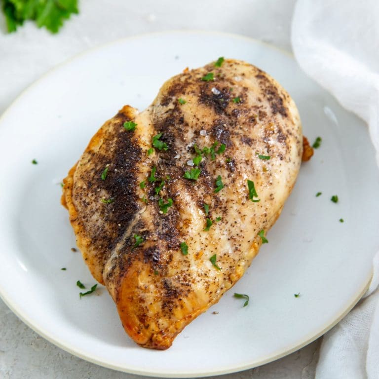 white plate with chicken breast on it. parsley in the back. white towel next to it.