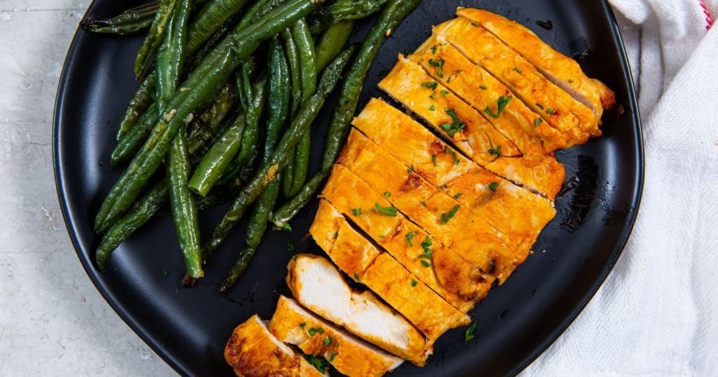 black plate with a chicken cut-up fork on the plate. green beans on the plate