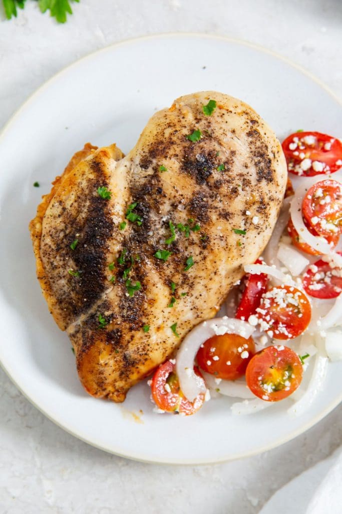 chicken on a plate with tomato salad next to it parsley in the back