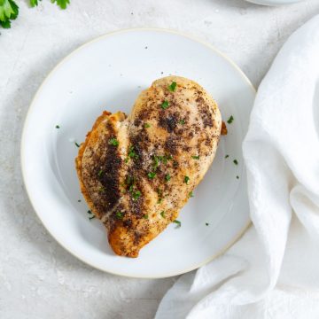 white plate with chicken breast on it. parsley in the back. white towel next to it.