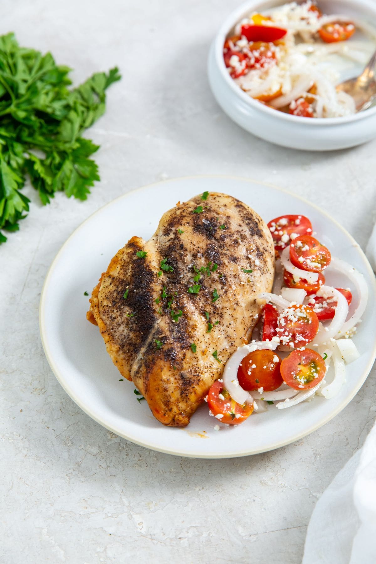 chicken on a plate with tomato salad next to it parsley in the back