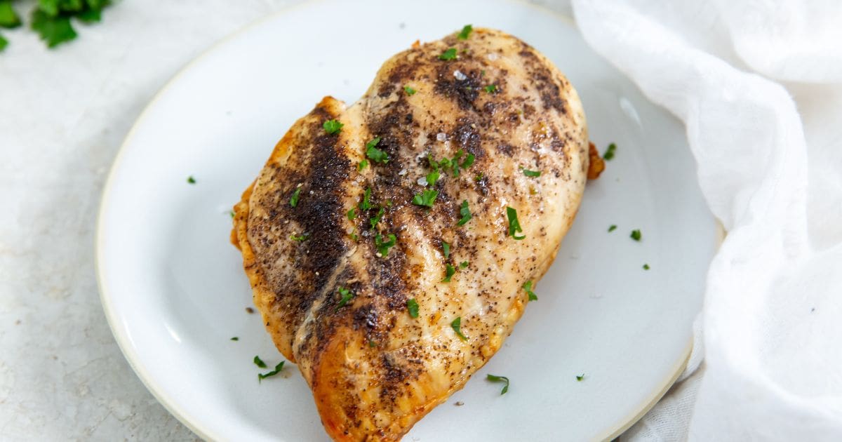 white plate with chicken breast on it. parsley in the back. white towel next to it.