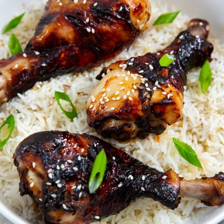 white bowl with rice and chicken legs inside. green onions in the back. Green towel next to bowl.