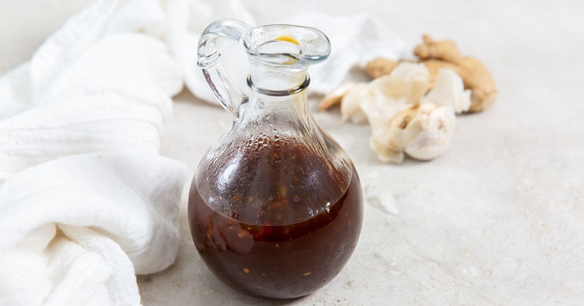 glass dressing bottle with teriyaki sauce inside white napkin in the back along with fresh garlic and ginger