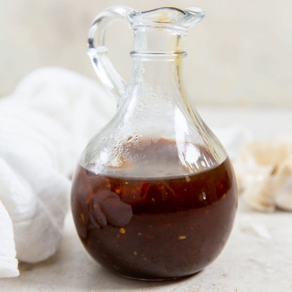 glass dressing bottle with teriyaki sauce inside white napkin in the back along with fresh garlic and ginger