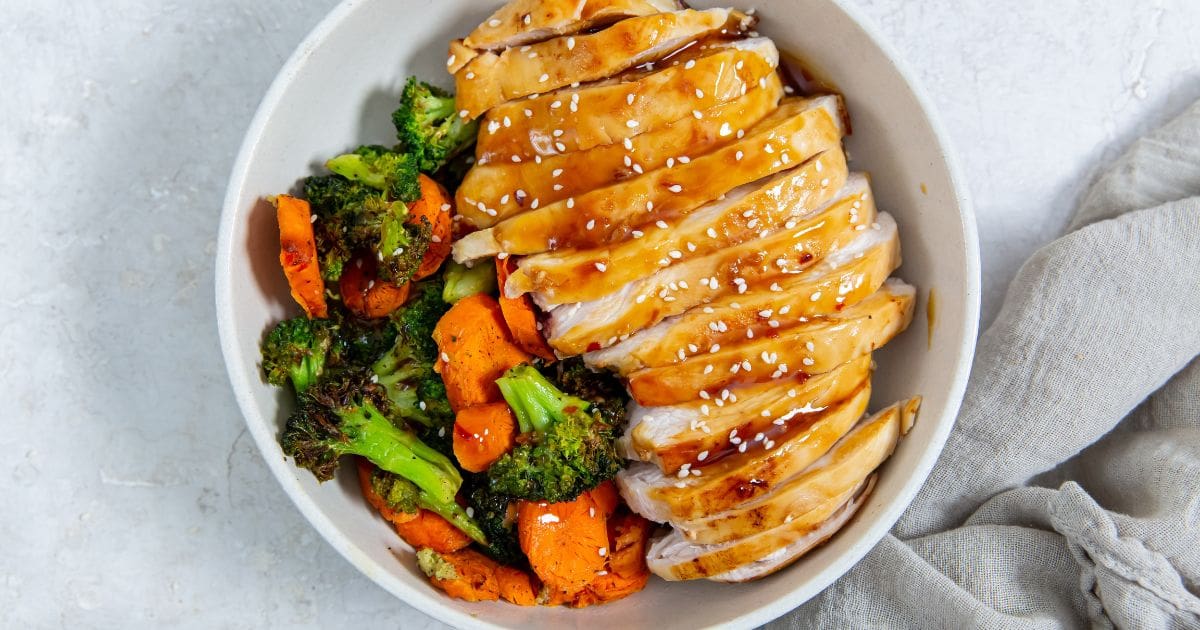 white bowl with chicken veggies and rice inside. gray towel next to it