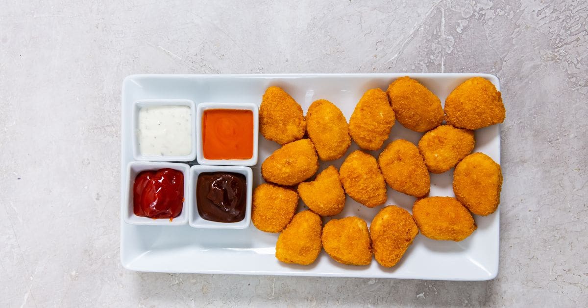 white plate with chicken nuggets dipping sauce in the back(buffalo, ranch, ketchup, and bbq)