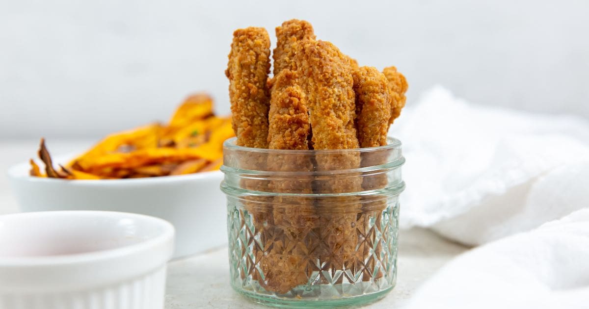 chicken fries inside a mason jar ketchup up front and sweet potatoes in the back. white towel next to it