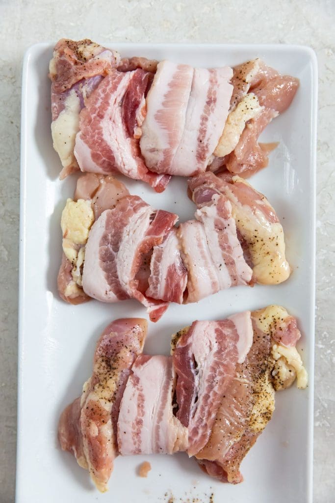 chicken wrapped in bacon on a white plate.