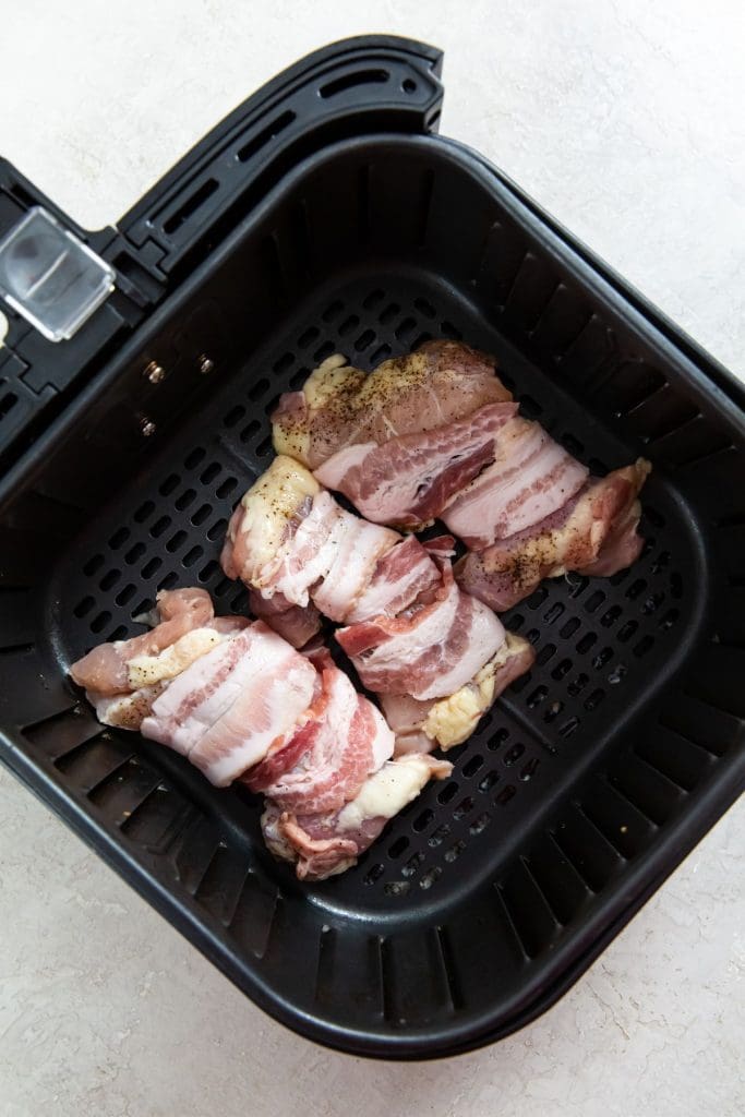 black air fryer with raw chicken inside.