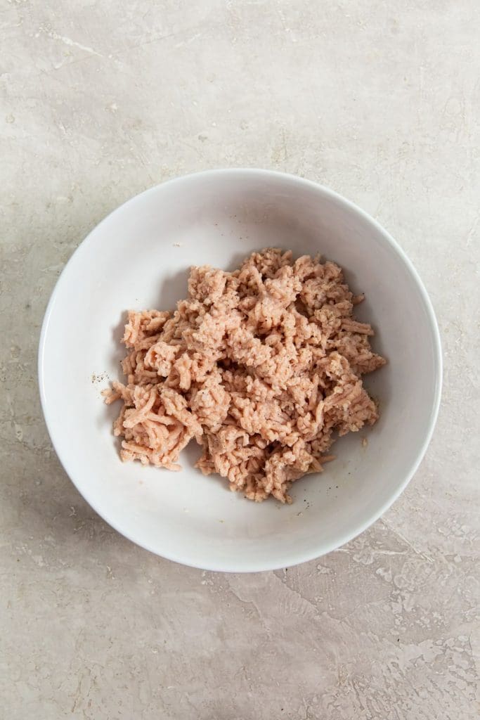 white bowl with raw chicken inside