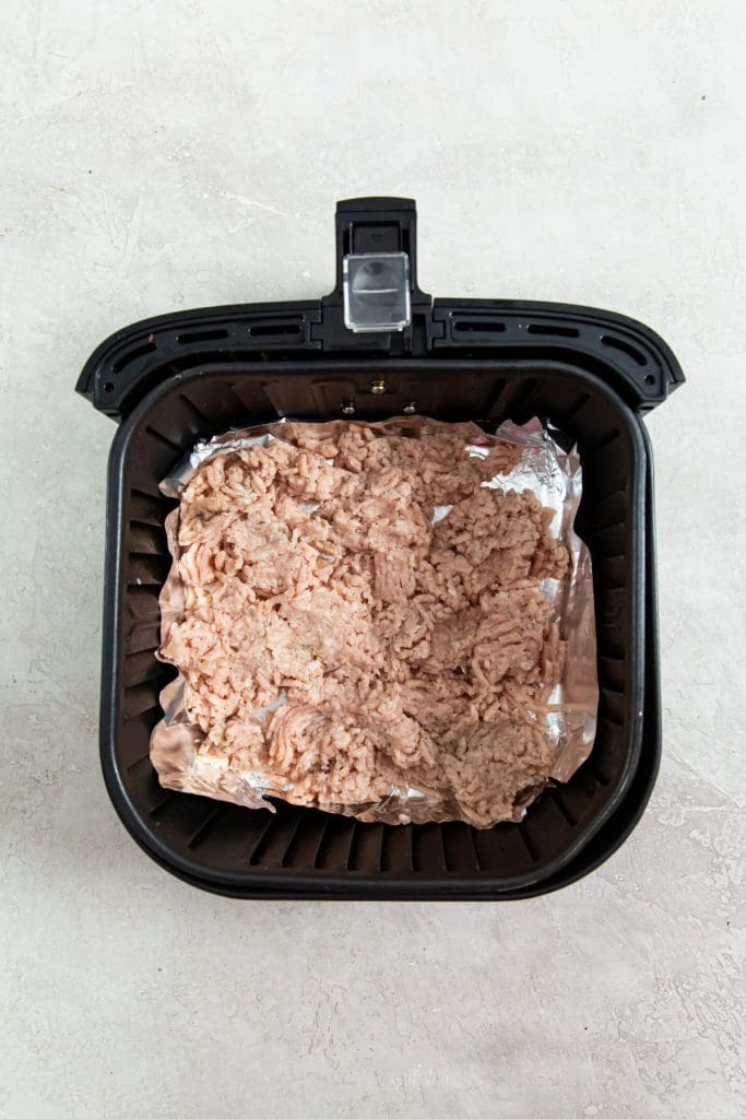 black air fryer basket with raw chicken and aluminum foil inside