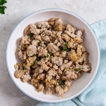 white bowl with chicken inside it.. blue towel and parsley in the back