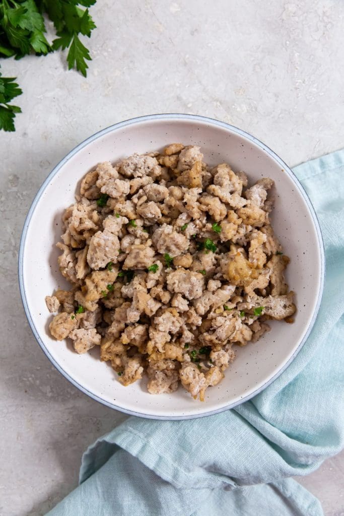 white bowl with chicken inside it.. blue towel and parsley in the back