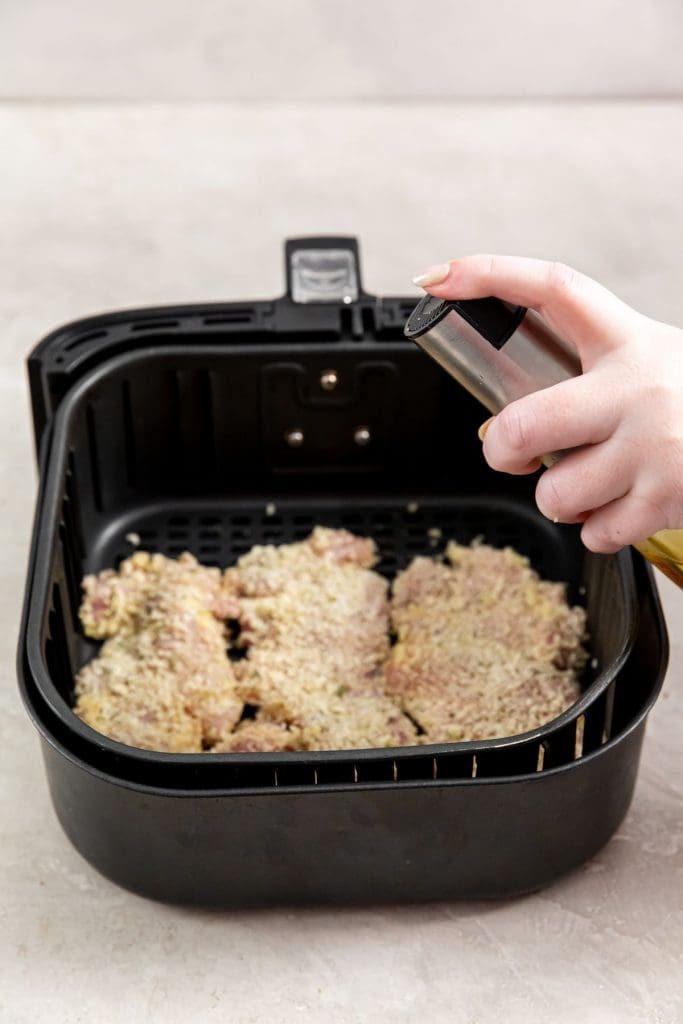 black air fryer with raw chicken inside. Getting sprayed with avocado oil