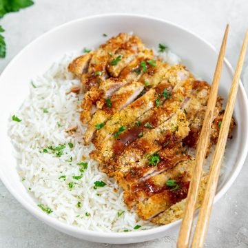 chicken and rice in a white bowl. chopsticks on the side of the bowl parsley and white towel in the back