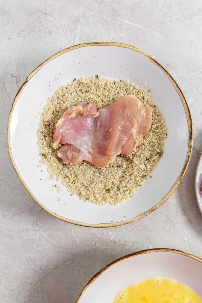 glass bowl with chicken thighs in bread crumbs