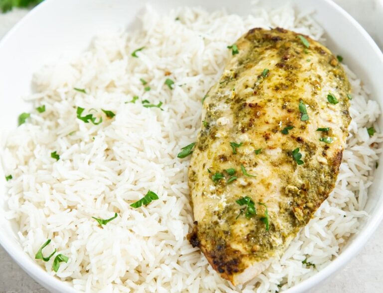 two plates one has just chicken the other has chicken and rice. parsley and pesto in the back.