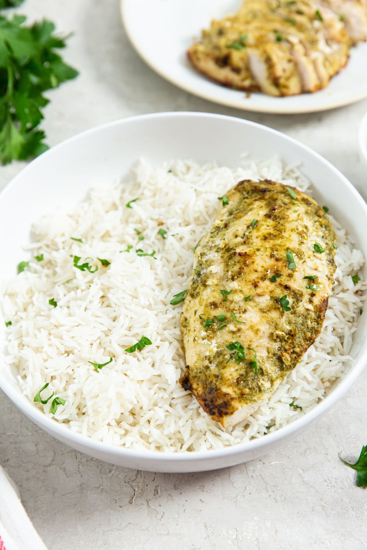 two plates one has just chicken the other has chicken and rice. parsley and pesto in the back.