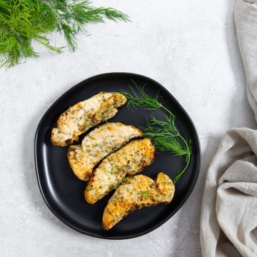 black plate with air fryer ranch chicken tenders and dill on it. dill and towel in the back